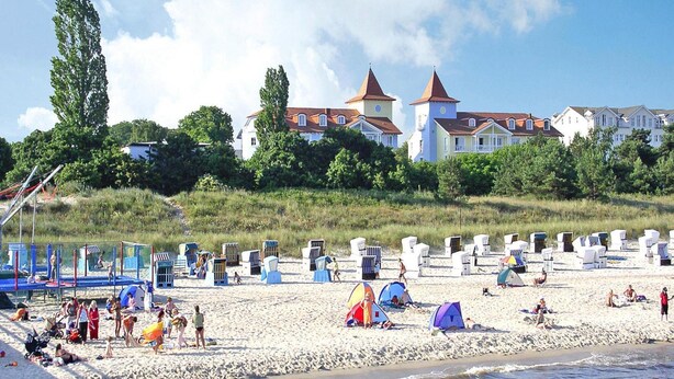 A beach with tents and beach chairs, a sandy shore, and buildings in the background. - Appartementhaus, Zinnowitz (Zinnowitz)