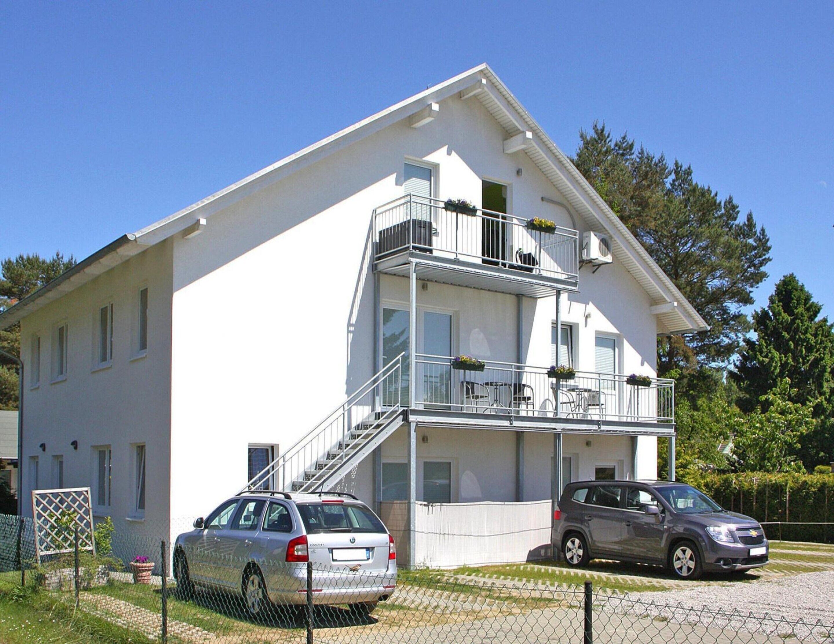 A two-story building with a balcony on the upper floor, a staircase leading to the entrance, and a car parked in front.