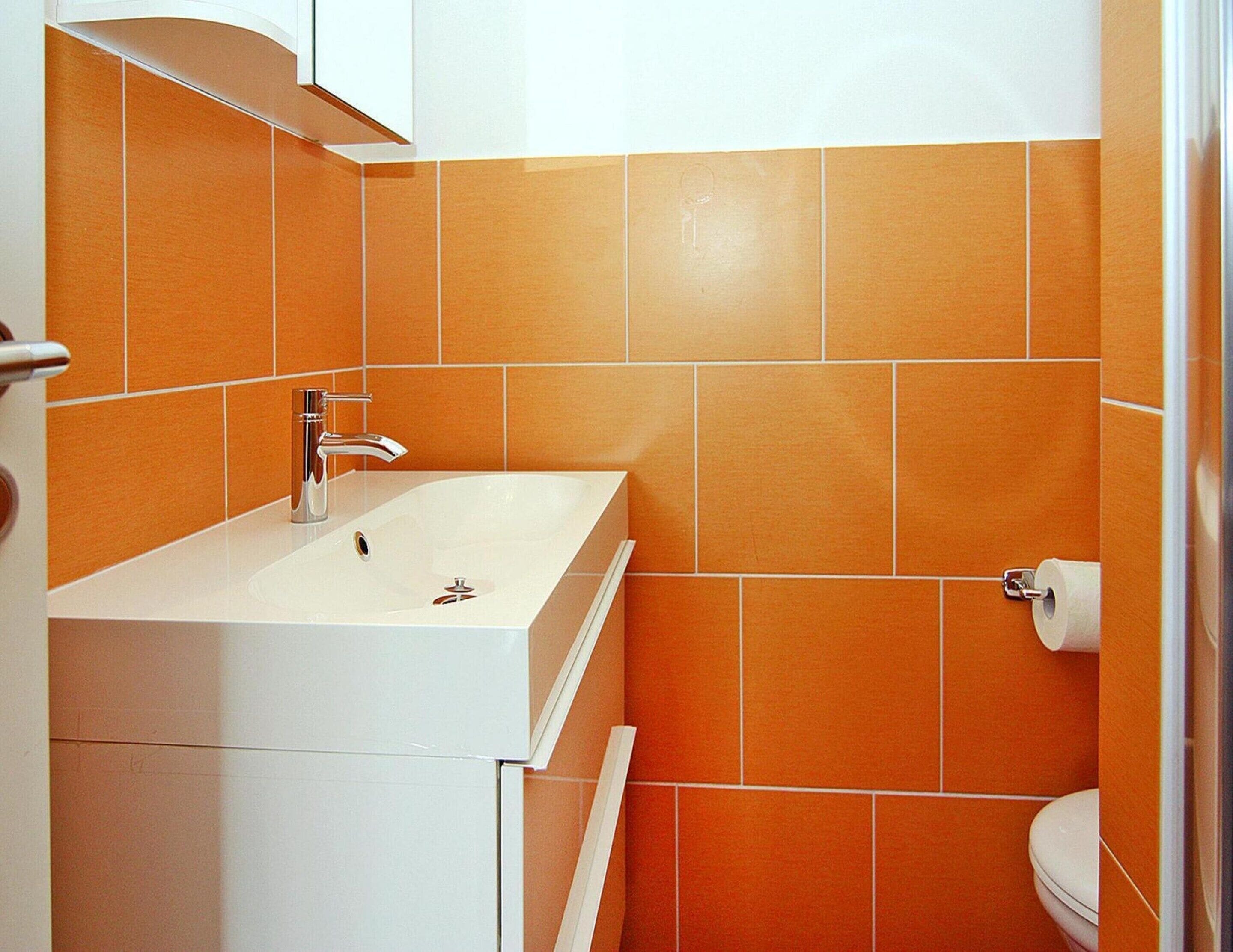 A bathroom with a white sink, orange tiles, and a toilet.