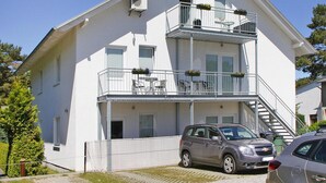 A two-story building with a balcony on the upper floor, a staircase to the upper level, and a car parked in front. - Appartementhaus, Zinnowitz (Zinnowitz)