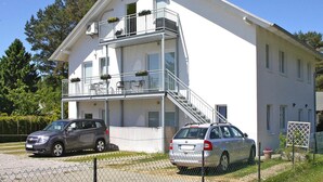 A two-story building with a balcony on the upper floor, a staircase leading to the upper level, and two cars parked in front. - Appartementhaus, Zinnowitz (Zinnowitz)
