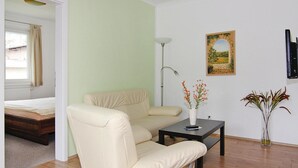 A room with a beige sofa, a small table with a vase of flowers, a painting on the wall, and a bed in the background. - Appartementhaus, Zinnowitz (Zinnowitz)