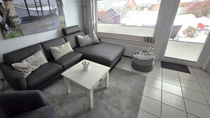 Ein modernes Wohnzimmer mit einer schwarzen Couch, einem weißen Couchtisch und einem grauen Teppich.