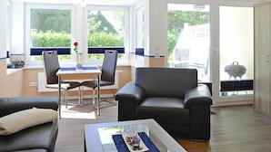 A modern living room with a sofa, a coffee table, and a dining area with chairs and a table. - Ferienwohnung in Wyk auf Foehr (Wyk auf Foehr)
