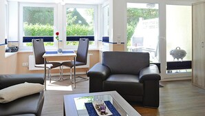 A modern living room with a sofa, a coffee table, and a dining area with chairs and a table. - Ferienwohnung in Wyk auf Foehr (Wyk auf Foehr)
