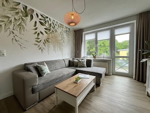 Un salon moderne avec un canapĂ© dâangle, une table basse en bois et une grande fenĂȘtre agrĂ©mentĂ©e de rideaux.