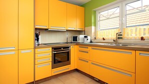A kitchen with yellow cabinets, a built-in oven, a microwave, and a window with curtains. - Appartementhaus am Kiessee, Westerholt (Nenndorf)