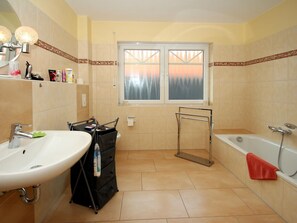 Un baño con lavamanos, bañera y ventana con vistas a árboles.