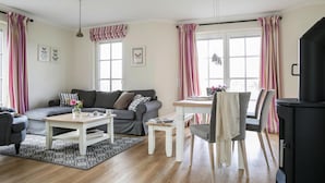 A cozy living room with a sofa, coffee table, and chairs, a dining table with a chair, and a black stove. - Haus an der Bodden-lagune mit Sauna (Fuhlendorf)