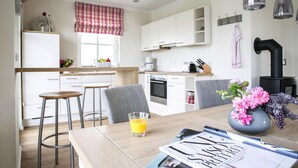 A modern kitchen with white cabinets, a dining table with two stools, a vase with flowers, and a glass of orange juice. - Haus an der Bodden-lagune mit Sauna (Fuhlendorf)