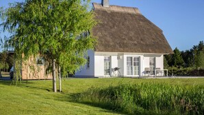 A white house with a thatched roof, a patio with a table and chairs, and a grassy lawn. - Haus an der Bodden-lagune mit Sauna (Fuhlendorf)