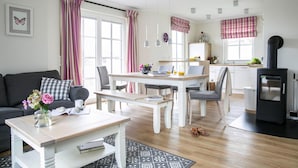 A modern living room with a sofa, coffee table, and dining area. There is a fireplace and a kitchen in the background. - Haus an der Bodden-lagune mit Sauna (Fuhlendorf)