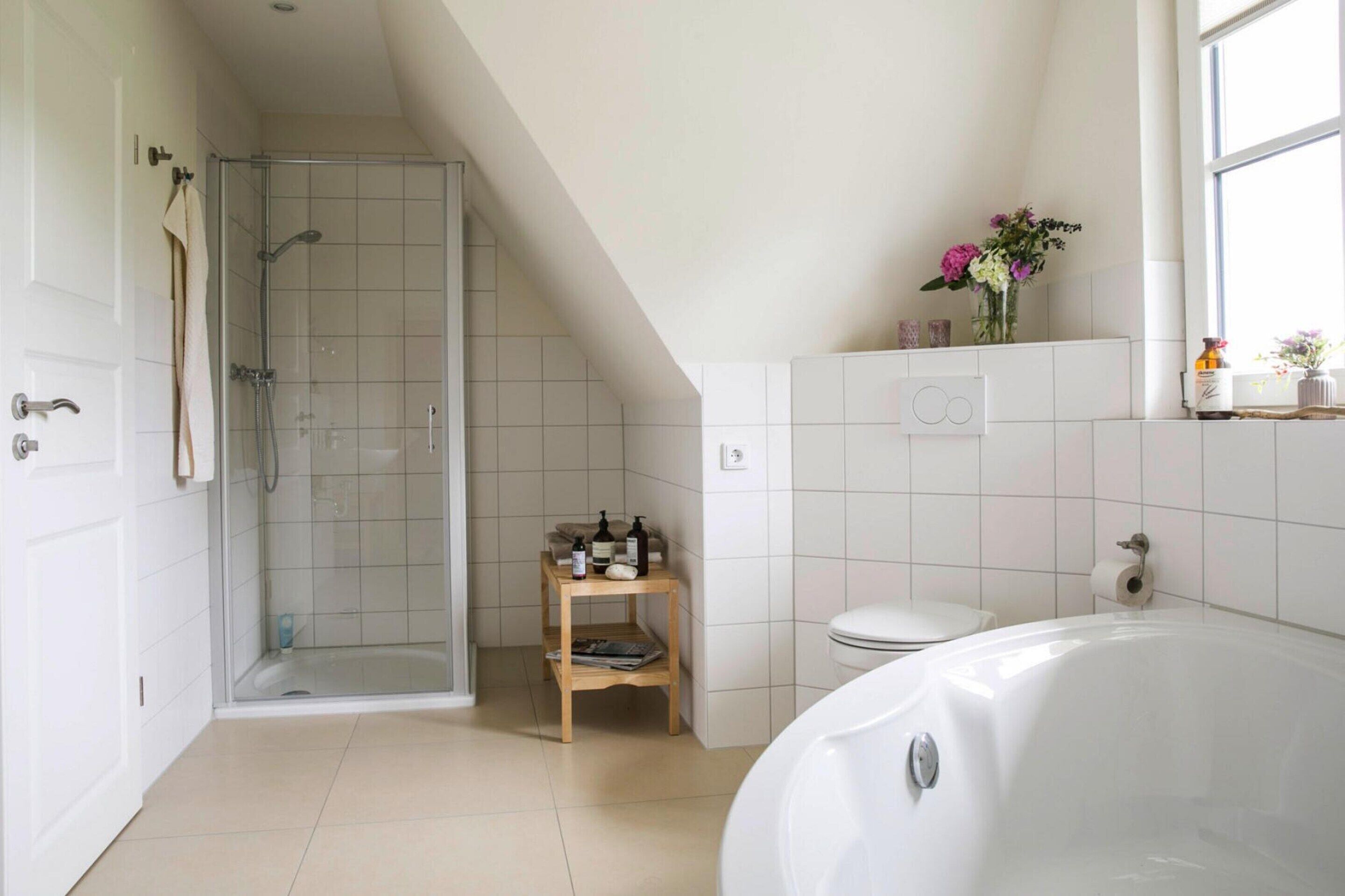 Et moderne badeværelse med bruseniche, toilet, badekar og en lille træhylde med toiletartikler.