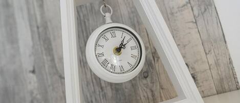 A white clock with Roman numerals in a white frame against a wooden background.