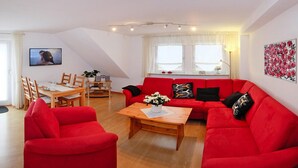 A living room with a red sofa, a wooden coffee table, and a dining table with chairs. - Holiday Home in Badenhausen (Bad Grund)
