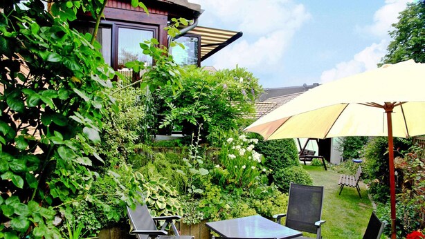 An outdoor patio with a table and chairs, surrounded by lush greenery and a wooden fence. - Holiday Home in Badenhausen (Bad Grund)