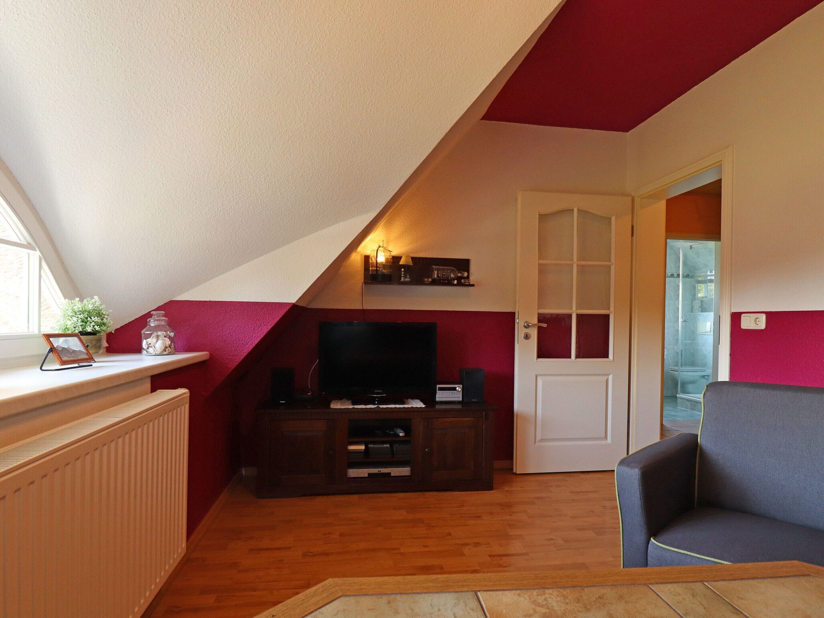 Ein gemütliches Dachzimmer mit Fernseher, einer Holz-Unterhaltungsecke und einem bequemen Sessel.