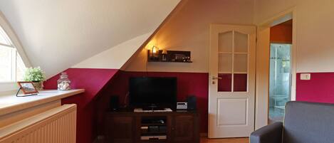 Ein gemütliches Dachzimmer mit Fernseher, einer Holz-Unterhaltungsecke und einem bequemen Sessel.