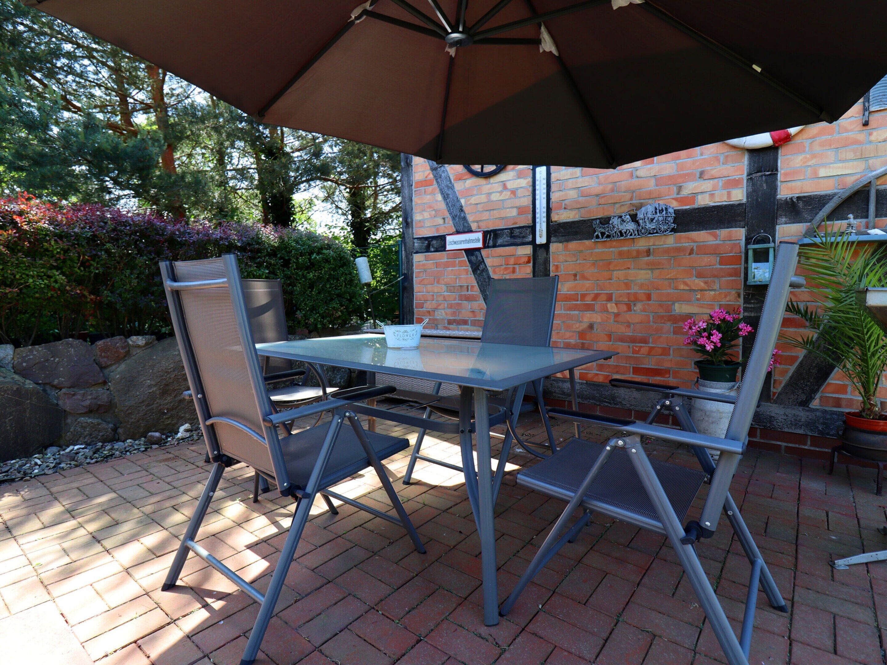 An outdoor patio with a table and chairs, a large umbrella, and a brick wall with greenery in the background.