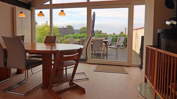 A dining area with a table and chairs, large windows, and a view of the outdoors. - Ferienhaus, Krusendorf (Schwedeneck)