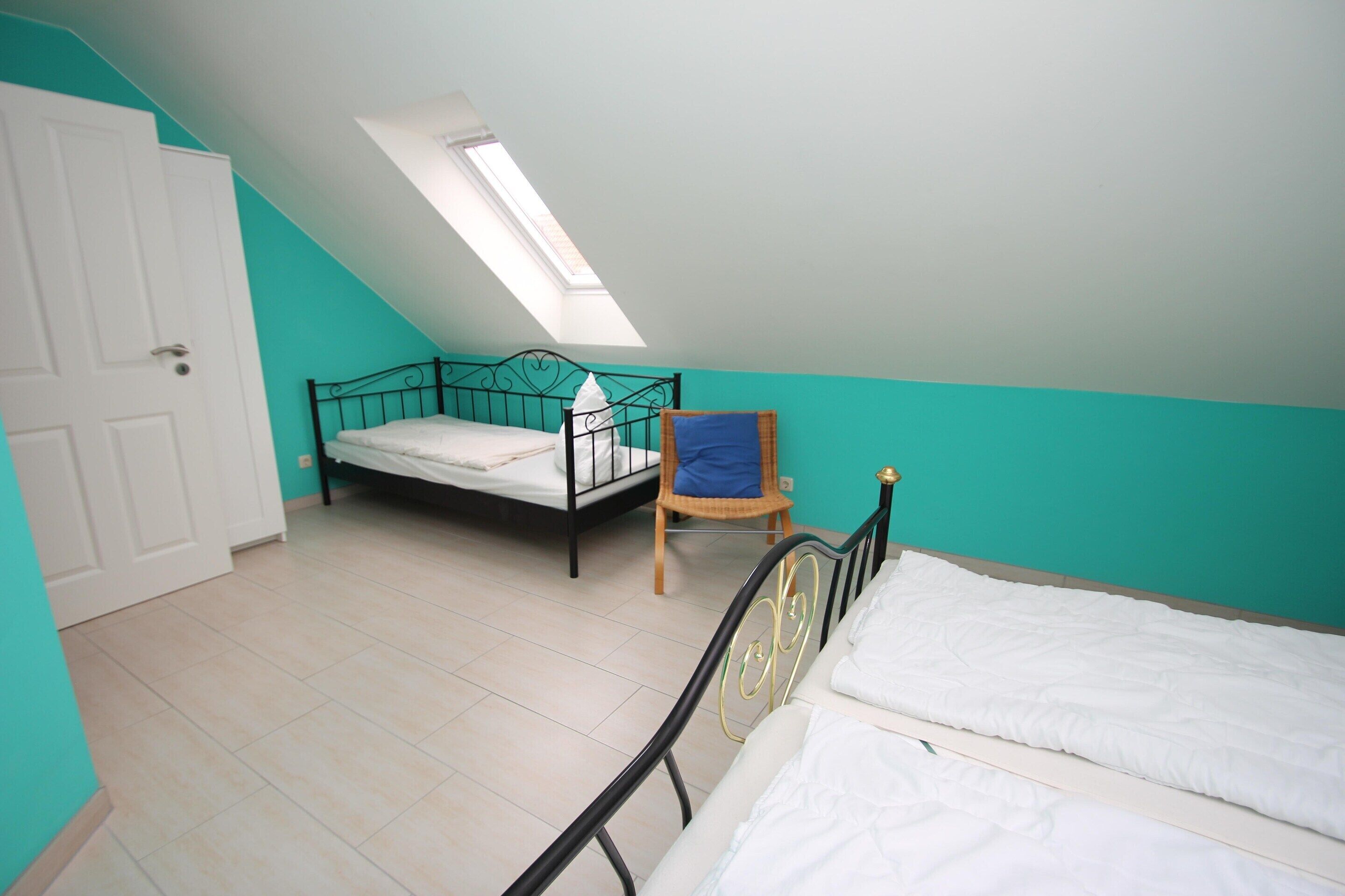 A bedroom with a skylight, a bed, a chair, and a door.