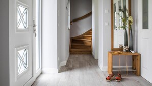 Un pasillo con una escalera de madera, una consola con espejo y un par de zapatos en el suelo.