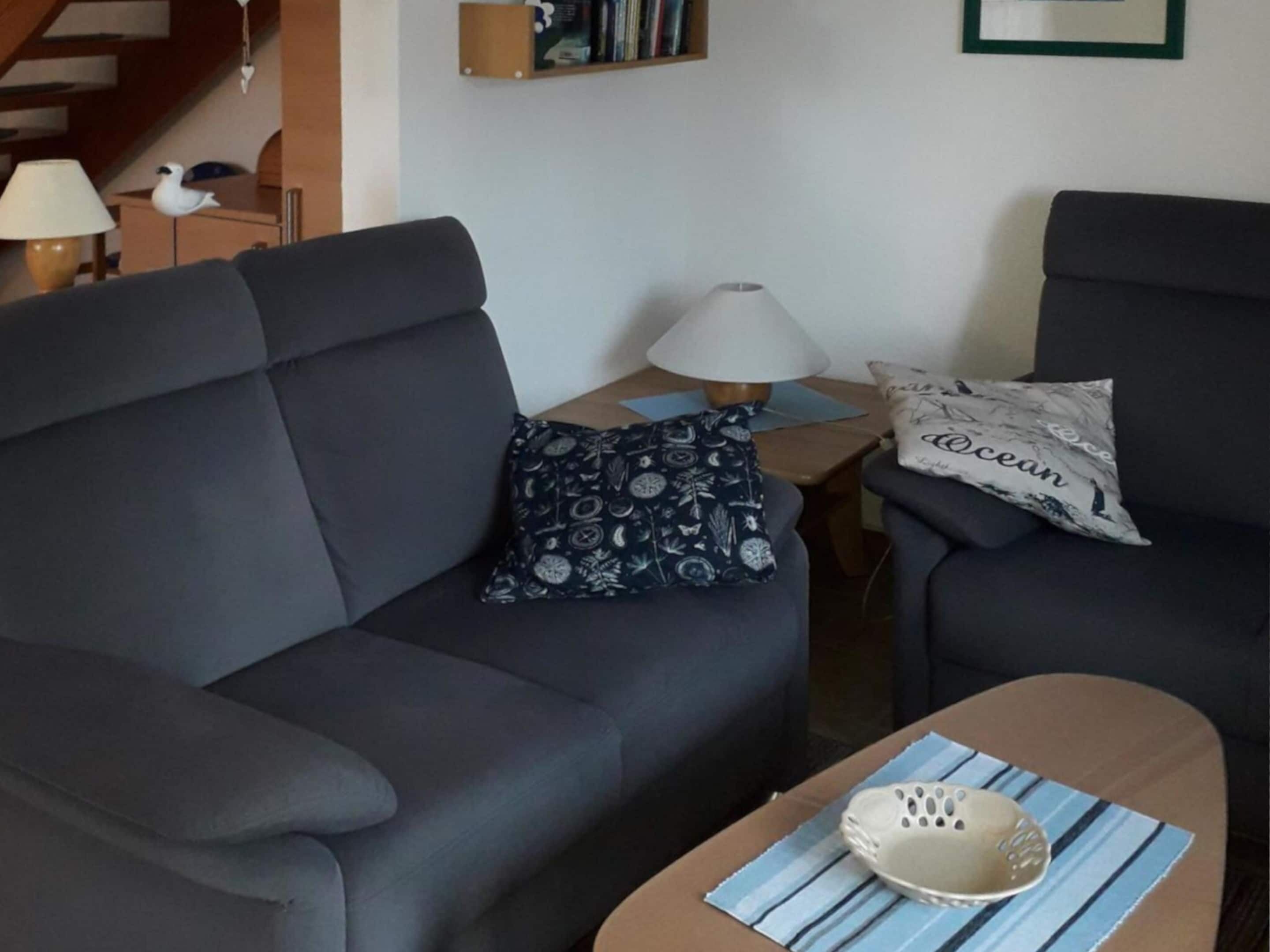 Un salon avec un canapé gris foncé, une petite table d’appoint avec une lampe et une table basse sur laquelle est posé un vase décoratif.