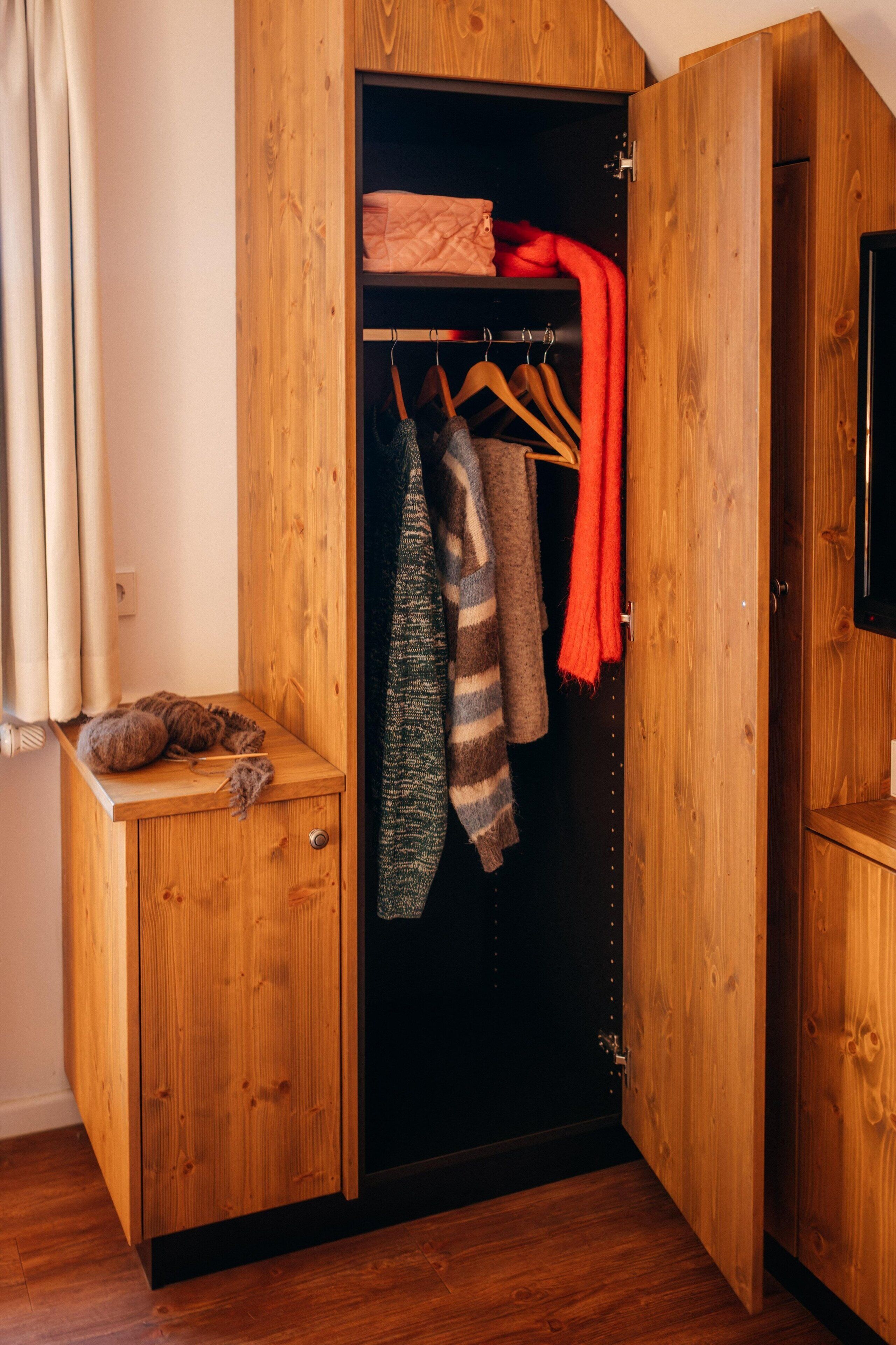 A wooden wardrobe with a hanging space for clothes and a small bench with a plush toy.