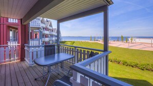 A wooden deck with a table and chairs, overlooking a beach and a grassy area with a fence. - Apartment in Rechin Right on the Water (Rechlin)