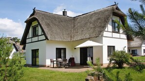 Une maison avec un toit de chaume, des murs blancs et un patio aménagé avec du mobilier d’extérieur.