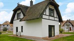 Il s’agit d’une maison traditionnelle avec un toit de chaume, des murs blancs et des éléments de décoration sombres. On peut y voir deux fenêtres et une cheminée.