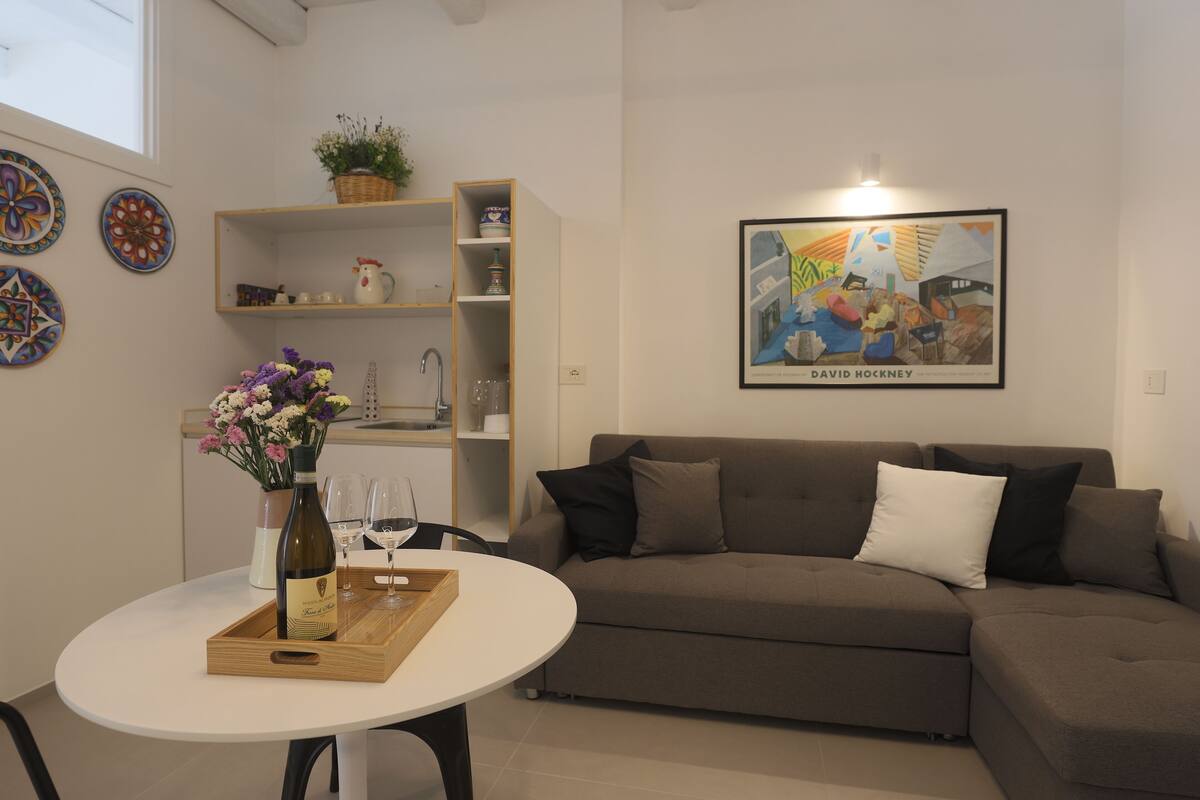A modern living room with a brown sofa, a white table, and a framed artwork on the wall.