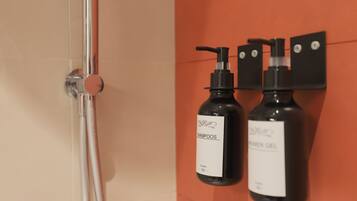 Ein Badezimmer mit Dusche und zwei Flaschen Shampoo und Duschgel an der Wand.