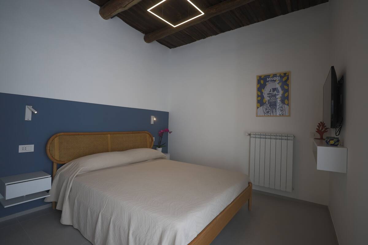 A bedroom with a bed, a nightstand, a wall-mounted TV, a radiator, and a poster on the wall.