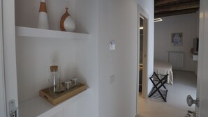A hallway with a wooden shelf holding glass bottles and a tray, leading to a room with a bed and a radiator. - DESIDERIO GUEST HOUSE (Salerno)