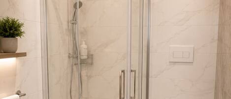 A modern bathroom with a glass-enclosed shower, a bidet, a toilet, and marble flooring.