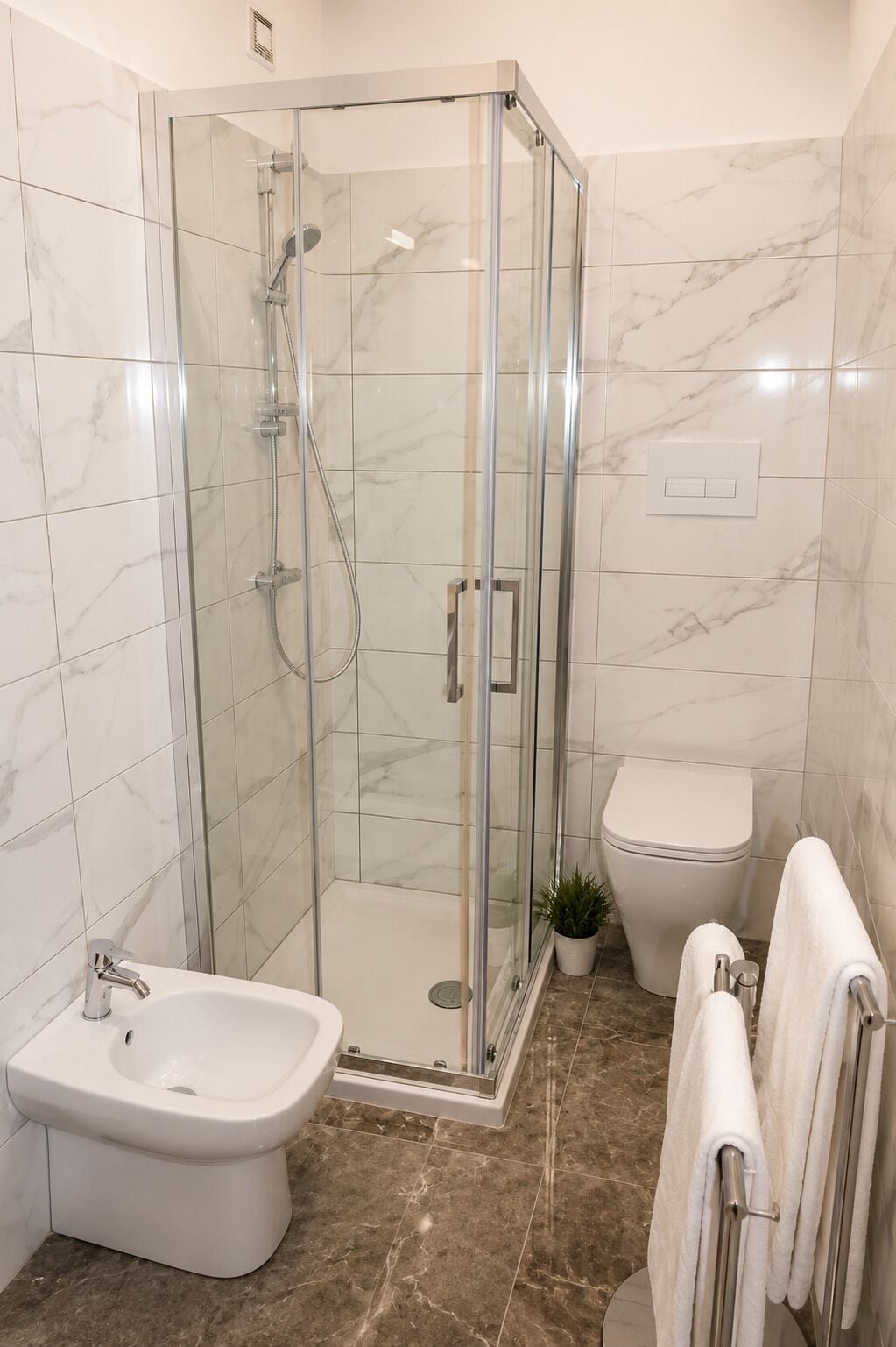 Un baño moderno con ducha de vidrio, un bidé, un inodoro y un perchero para toallas.