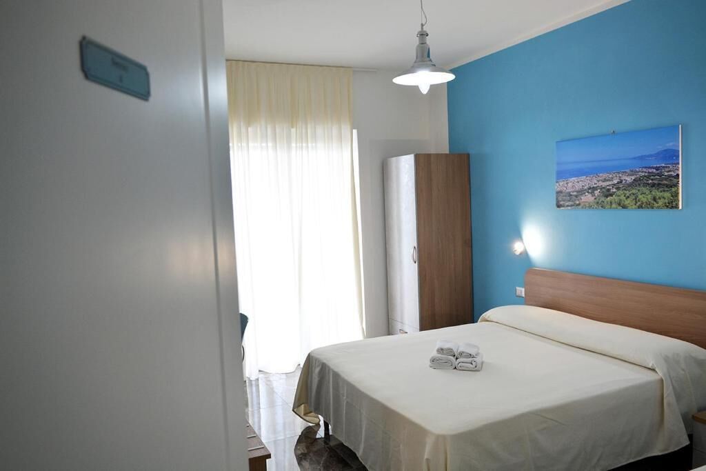 Ein Hotelzimmer mit Bett, einem Schrank, einem Bild an der Wand und einem Fenster mit Vorhängen.