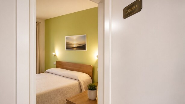 Un dormitorio con cama, mesita de noche con planta, cuadro en la pared y un letrero que dice 'CAMERA'.
