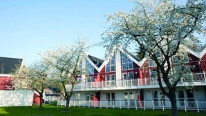Un edificio de varios pisos con fachada roja y blanca, balcones y un césped bien cuidado.