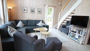 A modern living room with a grey sofa, two armchairs, a coffee table, and a TV on a white stand. There is a staircase to the right and a door leading outside. - Ferienhaus Seeidyll am Dummer See, Dummer (Dümmer)