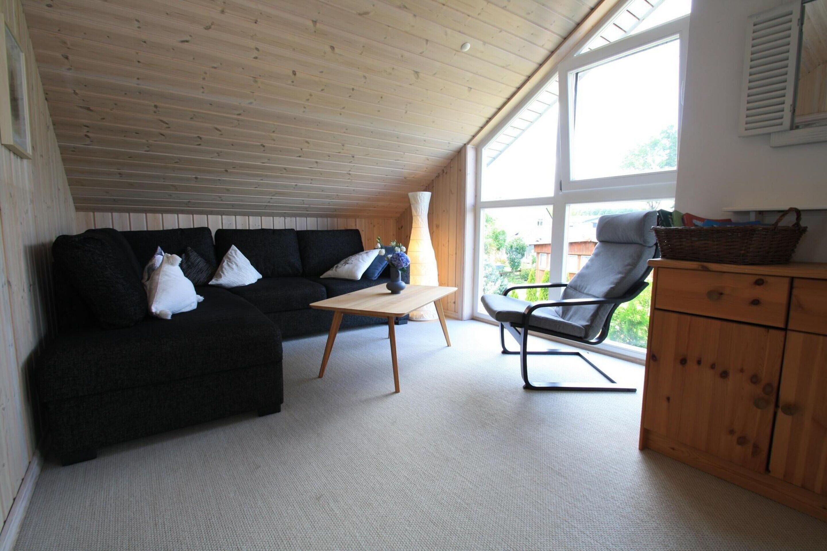 A cozy room with a black sofa, a wooden table, a chair, and a wooden cabinet.