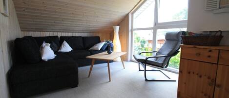 A cozy room with a black sofa, a wooden table, a chair, and a wooden cabinet.