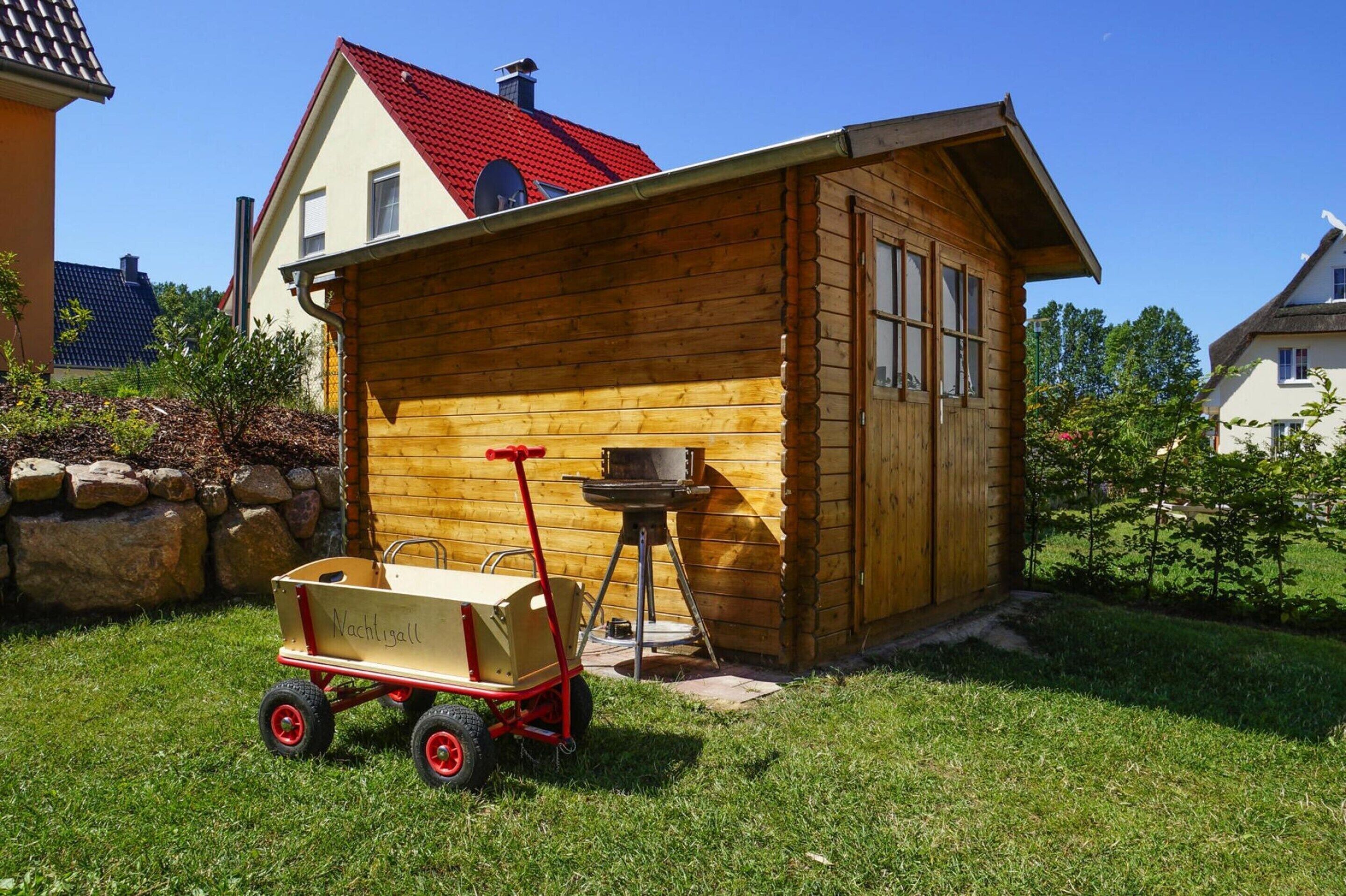 A wooden cabin with a red roof, a small porch, and a grill outside.