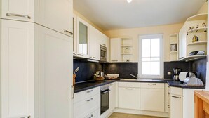 A modern kitchen with white cabinetry, a black countertop, and a window providing natural light. - Ferienhaus Nachtigall, Glowe (Glowe)