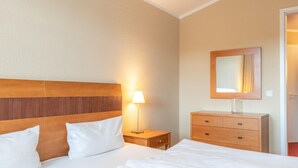 A hotel room with a wooden headboard, a bedside lamp, a wooden dresser, and a mirror. - Ferienwohnungen im Seepark Sellin (Sellin)