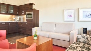 A modern kitchen with dark wood cabinets and a built-in oven. There is a beige sofa and a red armchair in the living area, with a wooden coffee table in between. - Ferienwohnungen im Seepark Sellin (Sellin)