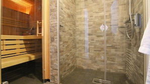 A glass-enclosed shower room with a stone wall and a wooden bench. - Ferienhauser im Torfhaus Harzresort, Torfhaus (Clausthal-Zellerfeld)