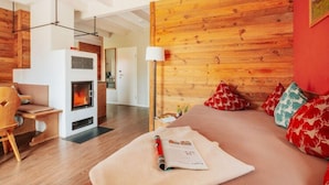 A cozy room with a wooden headboard, a fireplace, a bed with red and white patterned pillows, and a desk with a chair. - Ferienhauser im Torfhaus Harzresort, Torfhaus (Clausthal-Zellerfeld)