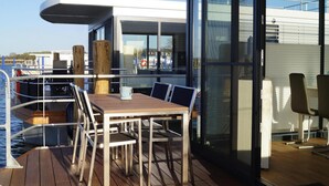 A modern deck with a wooden table and chairs, overlooking a marina with boats. - Hausboot Schwimmendes Haus in Ribnitz-damgarten (Ribnitz-Damgarten)